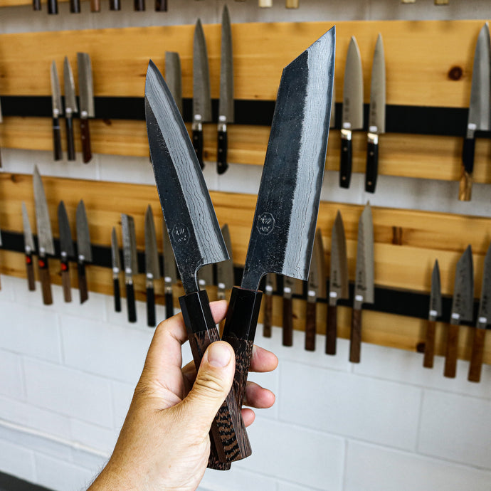 two hatsukokoro kumokage knives held in one hand, one is a petty knife the other is a bunka knife